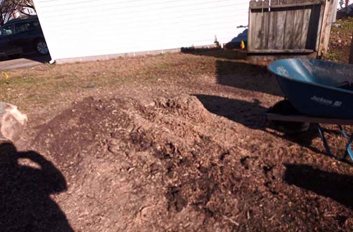Large pile of wood chips and debris left in a residential yard after a stump was professionally ground down into mulch by The Whole 9 Tree Service.