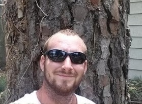 Trevor Hunt, owner of The Whole 9 Tree Service, standing in front of a tall pine tree scheduled for removal in Chesapeake, VA.